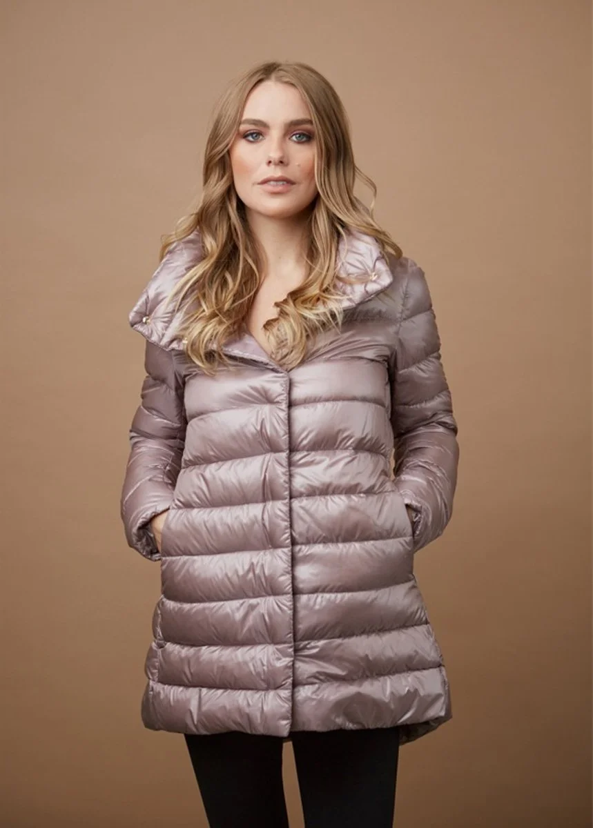 A woman with long, wavy blonde hair wearing a shiny, puffy, mauve-colored winter coat with a hood against a plain brown background.