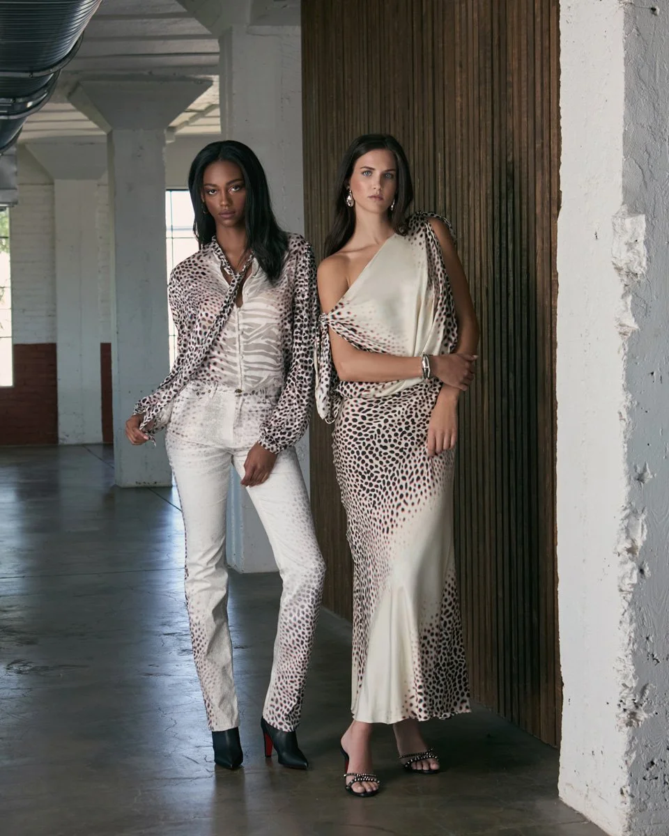 Two women wearing animal print clothing standing indoors against a wooden wall.