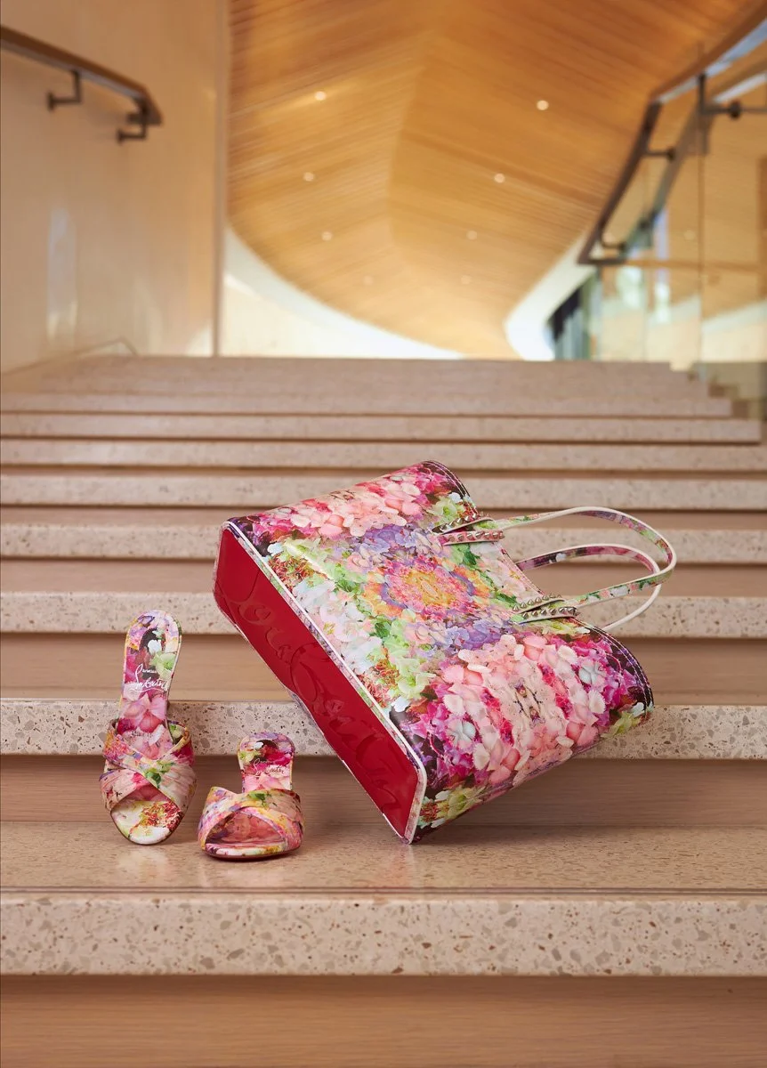 A floral handbag and matching shoes resting on wooden stairs in a well-lit, modern interior with wooden and glass design elements.