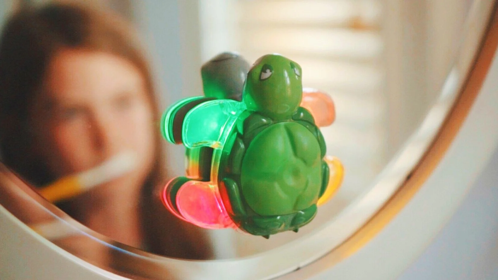 Child brushing teeth in mirror with green Toothbrushing Turtle Timer feet lit up
