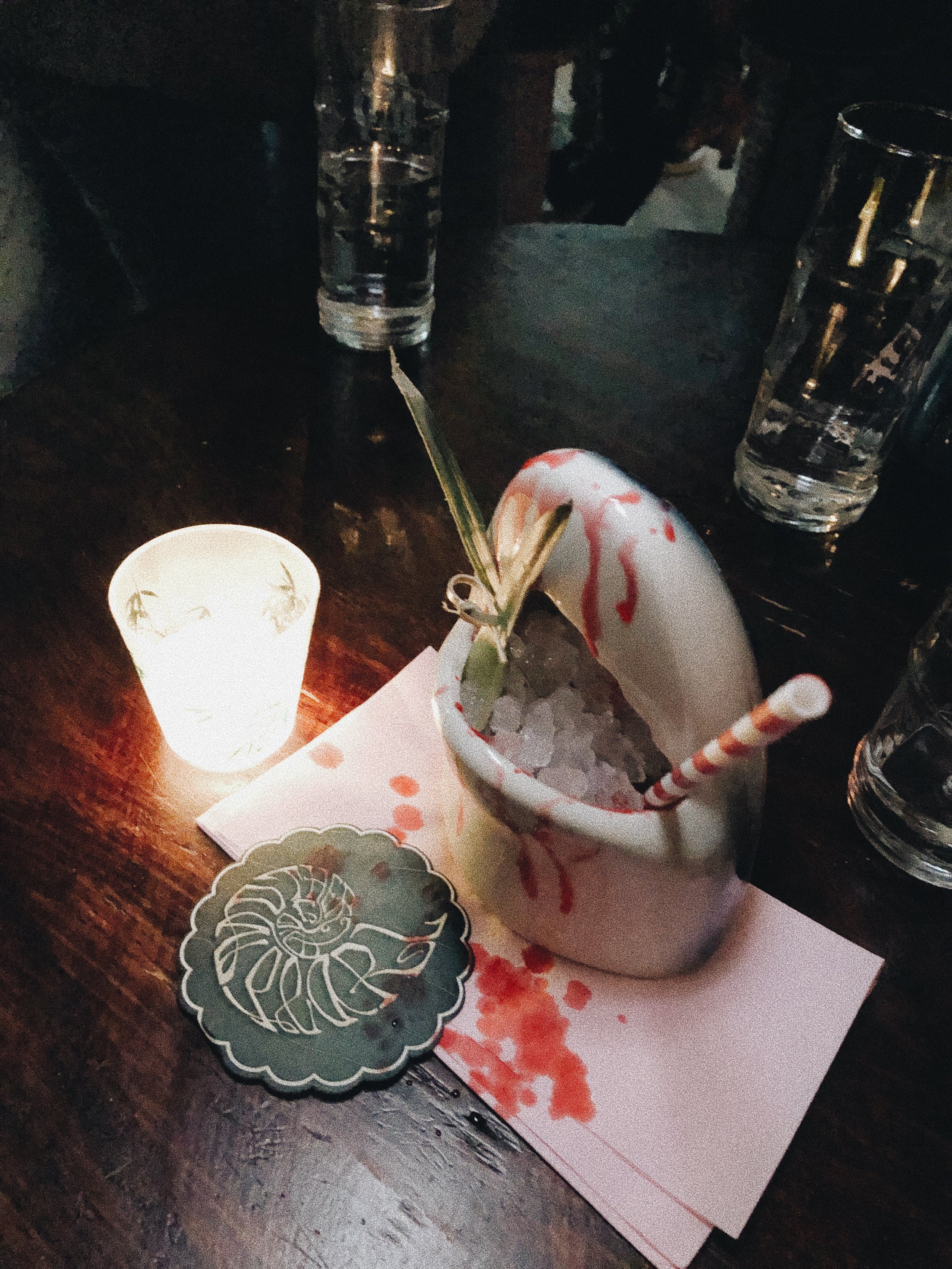 Candlelit cocktail garnished with herbs on a dark bar table.jpg