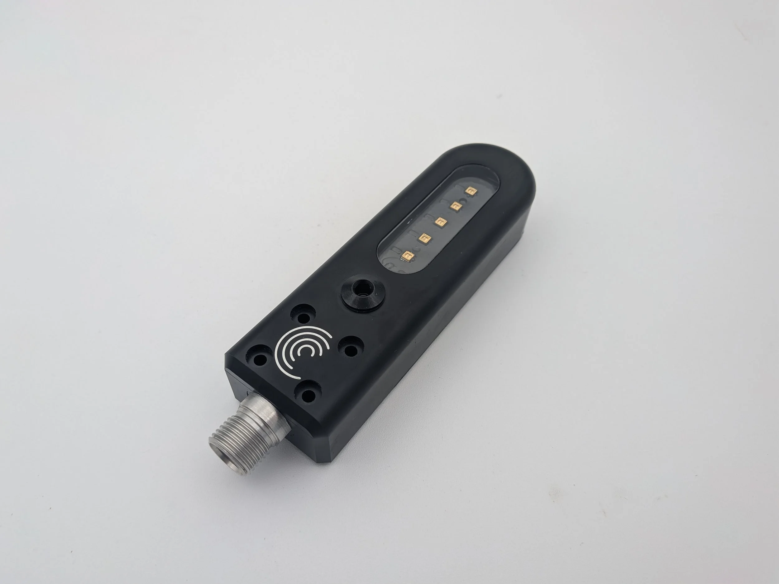 Black electronic device with a metal threaded connector at one end, a circular sensor, an icon indicating wireless or contactless communication, and a transparent window showing a series of small gold contact points inside