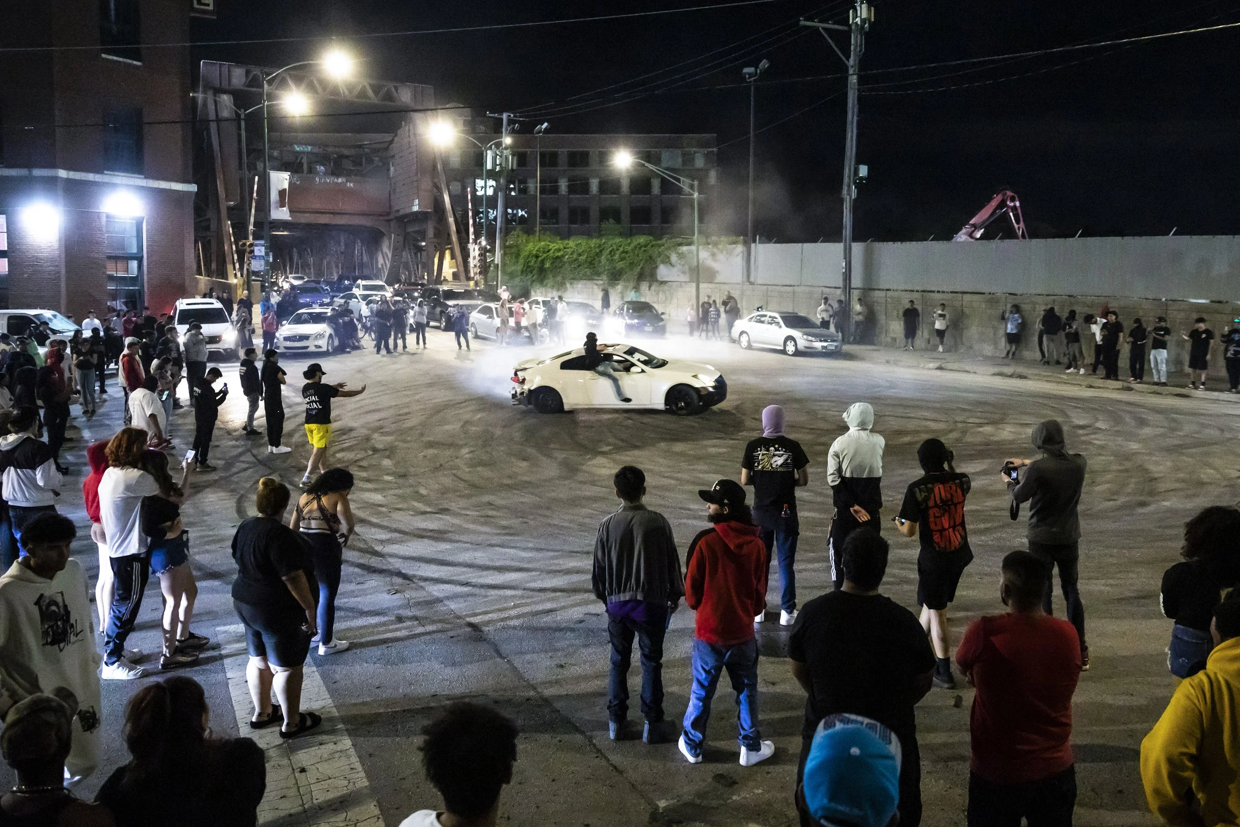  Passengers hang out the windows of a car as it drifts in circles during a takeover in a South Side intersection, Friday night, July 29, 2022.   These meets have long drawn complaints about the noise, the disruption and the danger. But, despite a rec