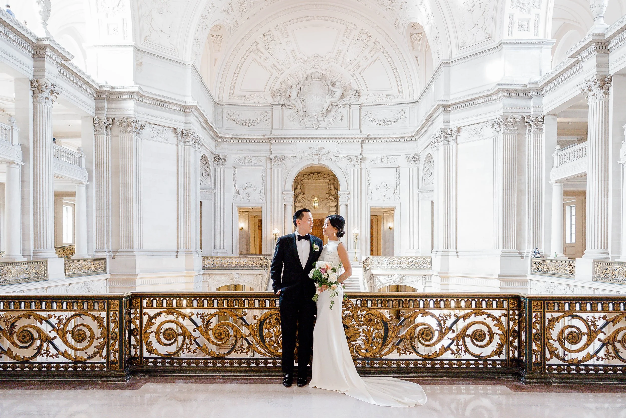 Bride and groom in elegant hall with ornate architecture and columns.