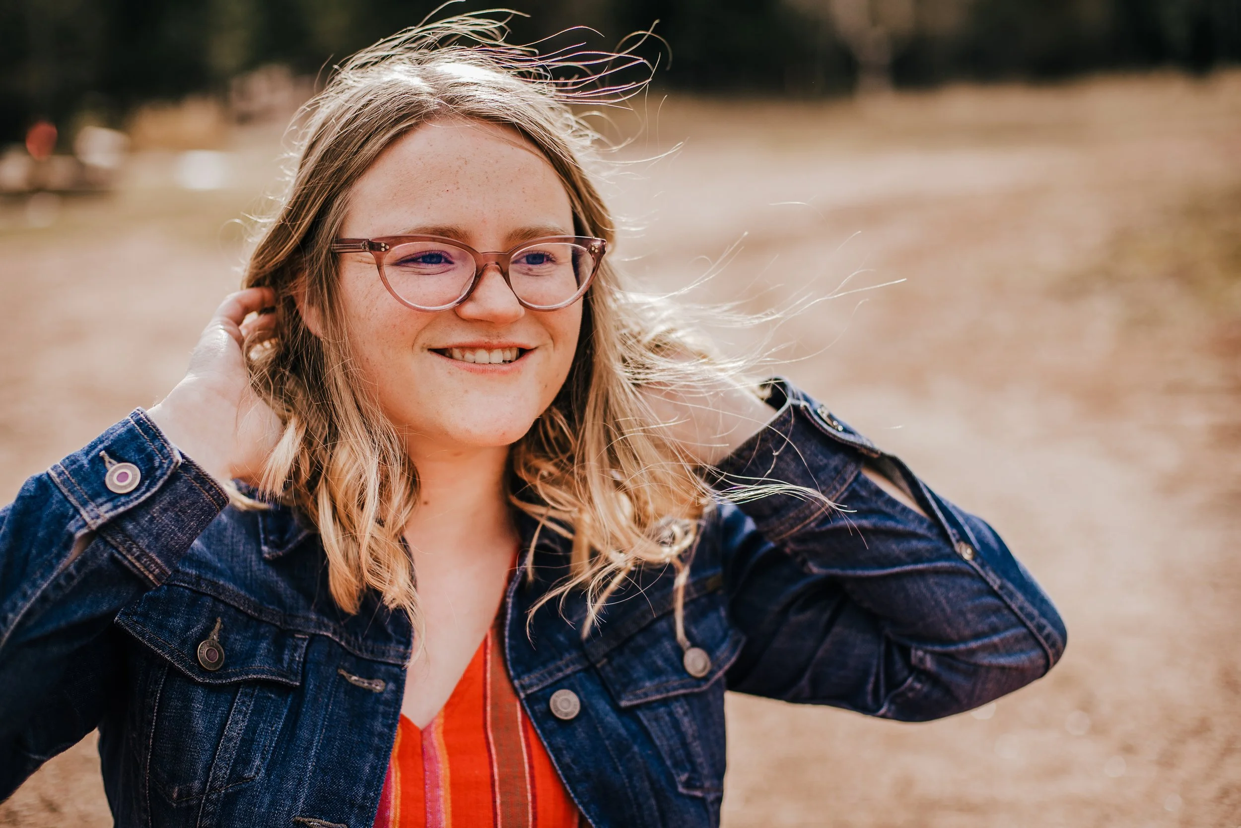 High school senior girl in denim jacket laughing in windy Colorado field — Denver senior portrait photographer Jennie Bennett Photography