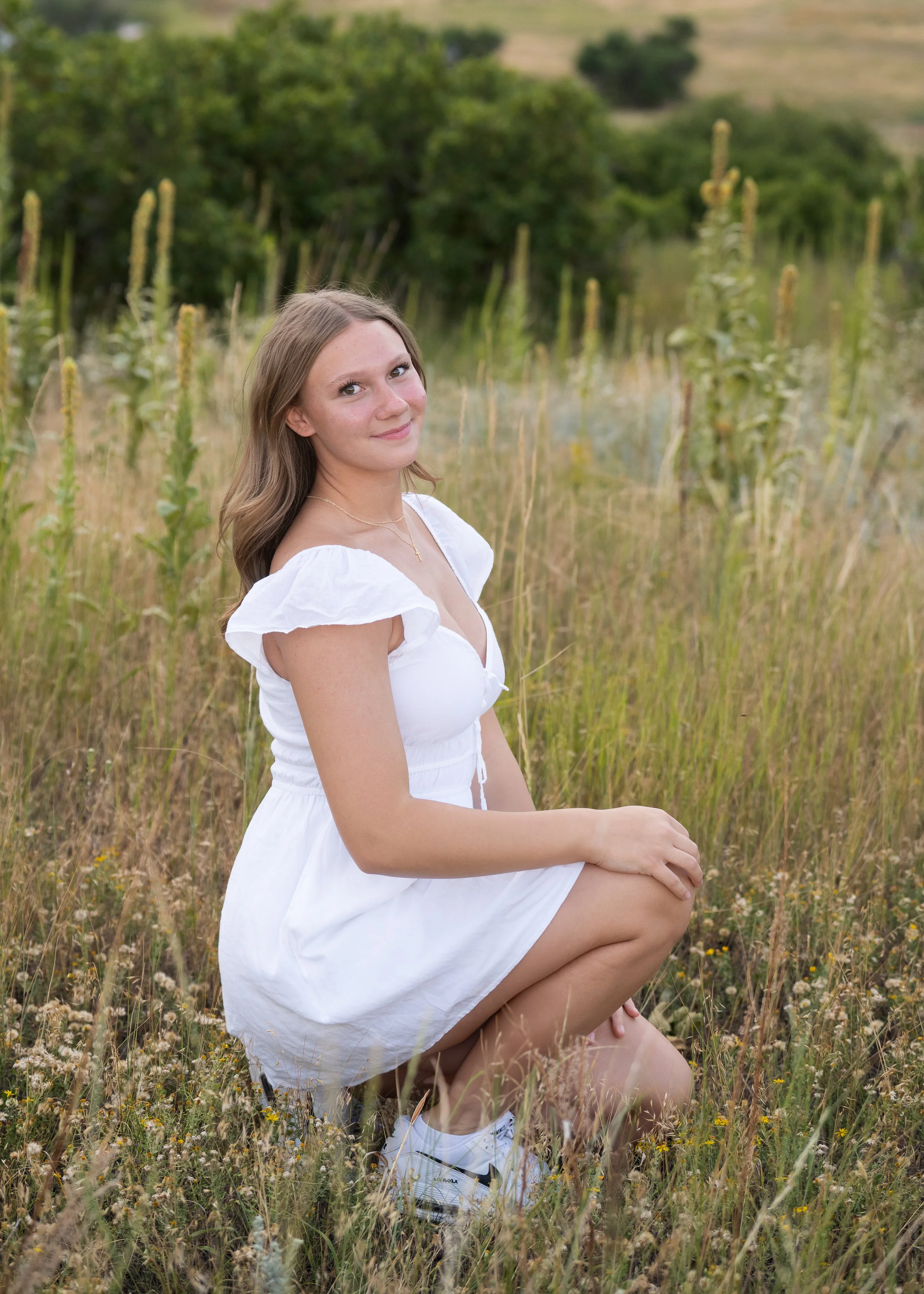 High school senior girl in white dress sitting in wildflower meadow with tall grasses — Castle Rock senior photographer Jennie Bennett Photography