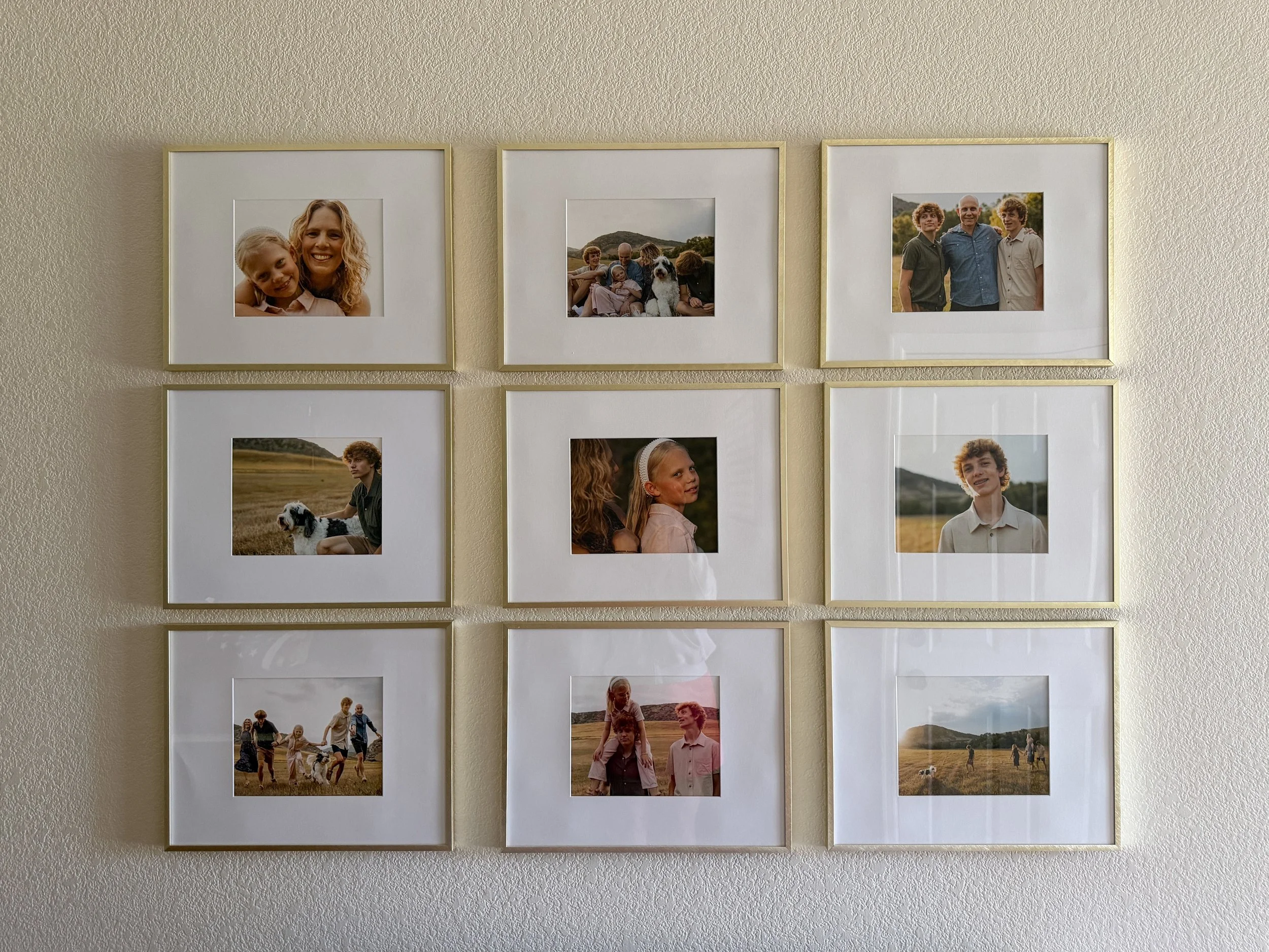 A closer view of a nine-frame gallery wall with gold frames and white mats showcasing professional family portraits