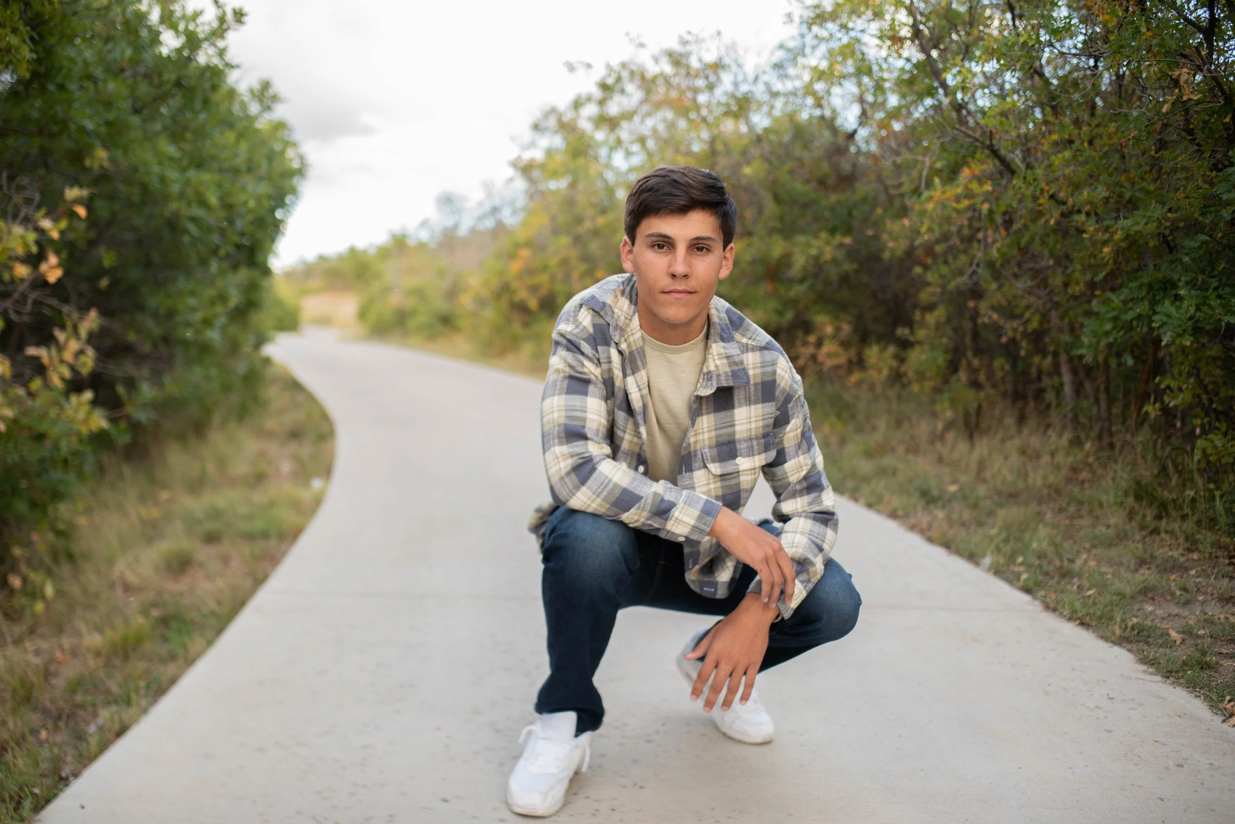 High school senior boy crouching on Colorado trail in plaid shirt — Denver senior portrait photographer Jennie Bennett Photography File: jennie-bennett-photography-denver-senior-portraits-colorado-trail-fall.jpg