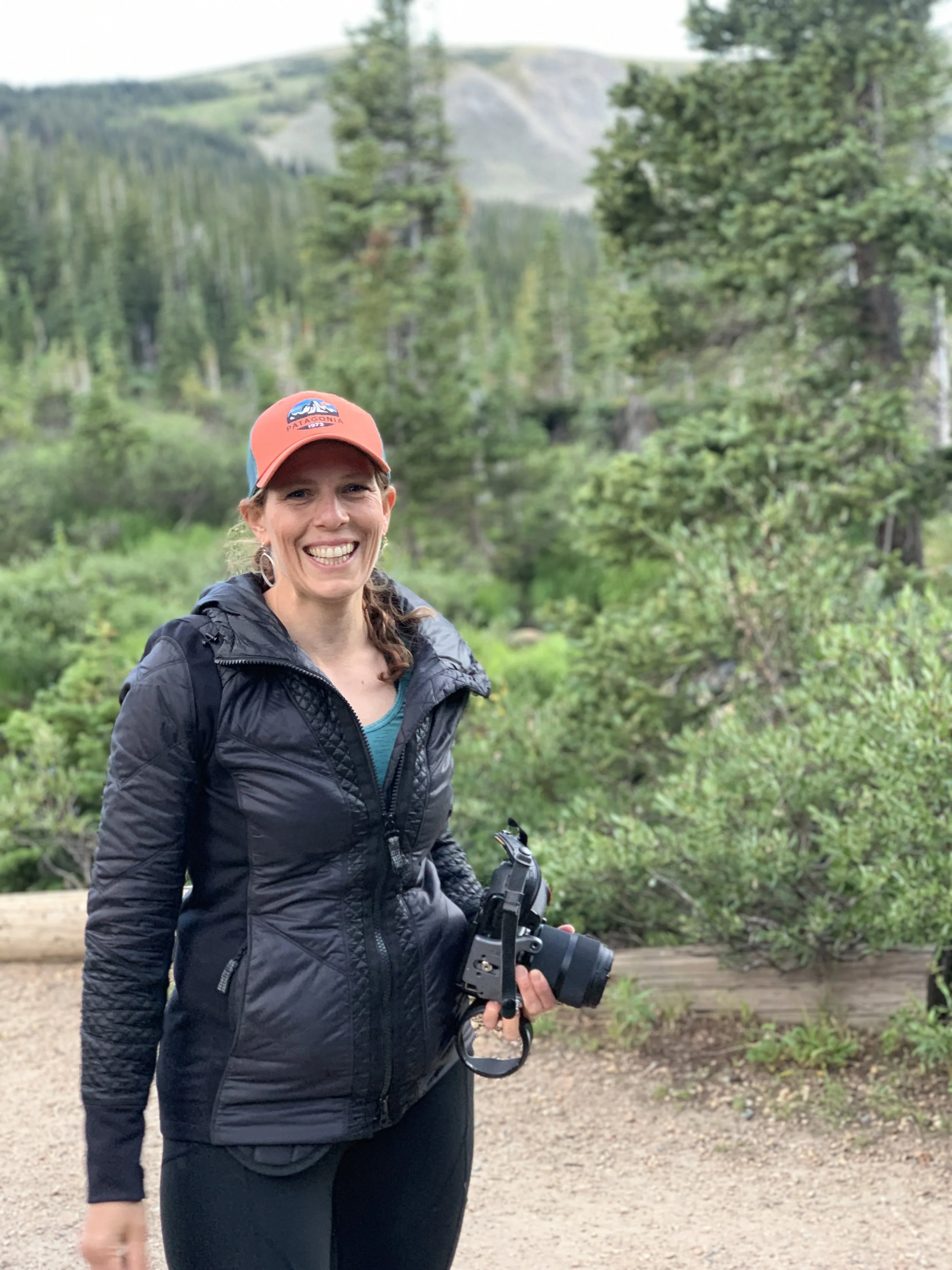 Jennie Bennett, Denver senior photographer, smiling with camera during a Colorado mountain session