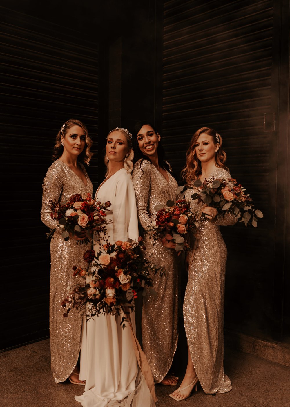 Lucy stands with her 3 bridesmaids who are wearing long sleeve gold sequin dresses. All the bouquets are full of autumnal coloured flowers and foliage.