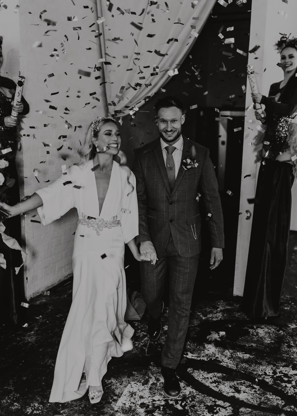 A black and white image of Lucy and Jody walking through confetti, both looking super happy!