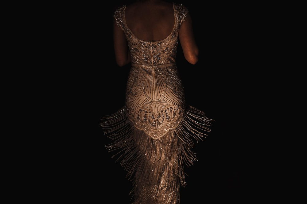  Against a dark background the image shows the back of Emma’s dress from the shoulders to below the knee. She is moving so all of the beaded tassels are in motion. 