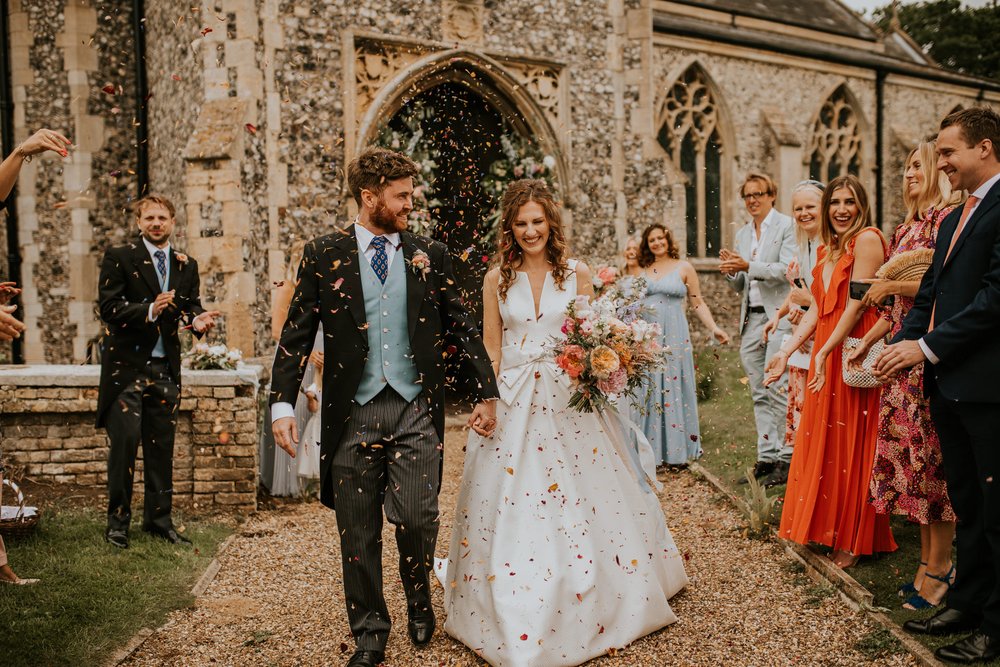  Tom and Steph are showered in confetti from guests as they walk down the path away from church. 