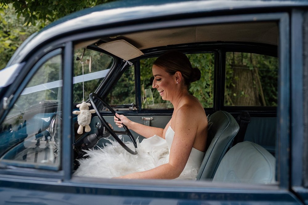  Sophie sits in the drivers seat of a 1969 Morris Minor navy blue car, putting the car in gear and getting ready to drive to the reception venue. 