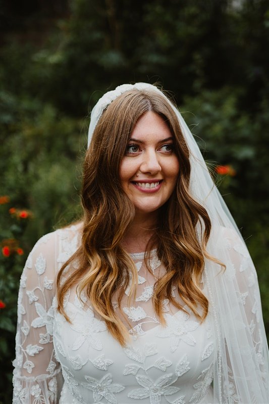  Gemma looks slightly away from the camera in a close up image. Her hair is down and wavy. You can see the detail of the beaded flowers all over her dress.  
