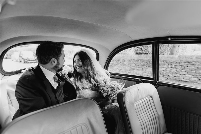  Gemma and Nick smile at each other in the back of a vintage wedding car. 