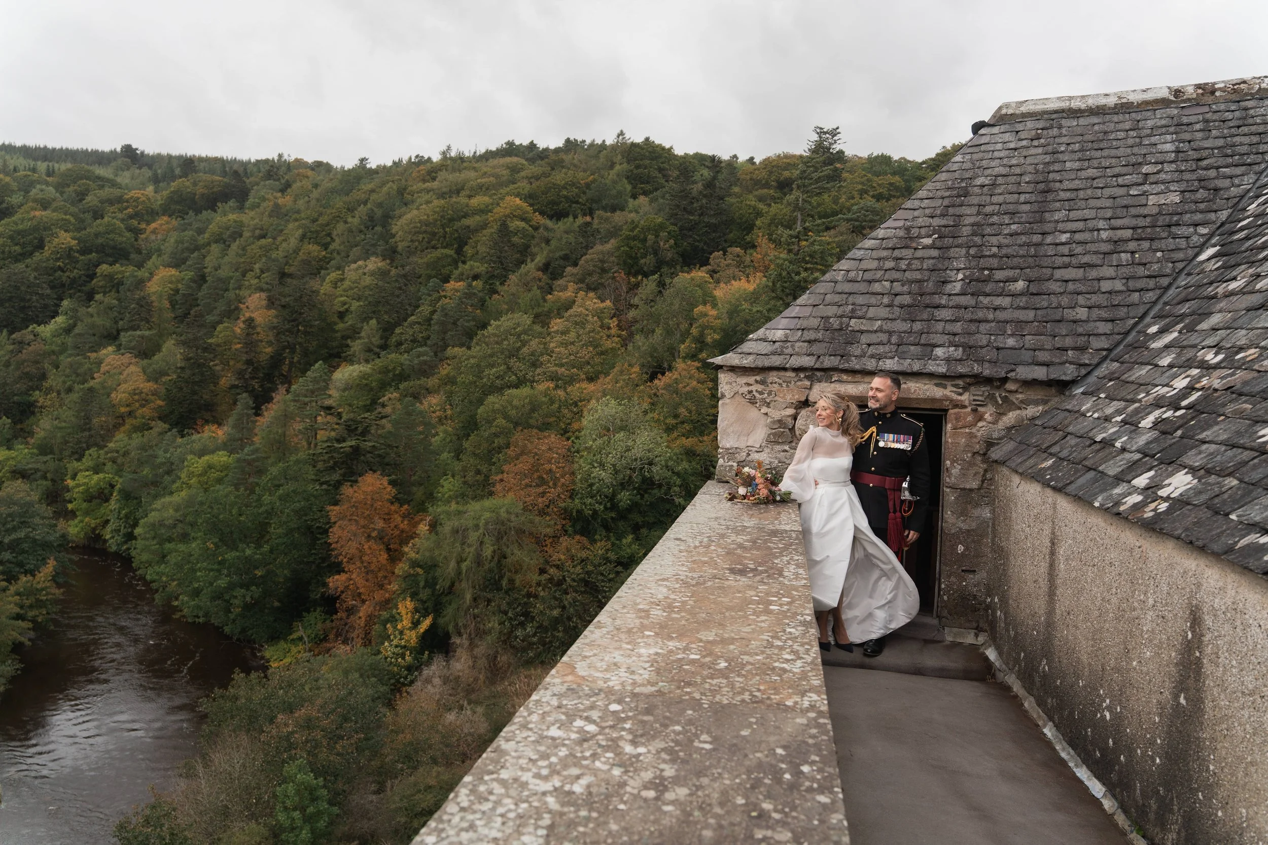 Bride Jaymie in a Jesús Peiró gown standing on the roof of Neidpath Castle in Scotland, with Karl her husband.