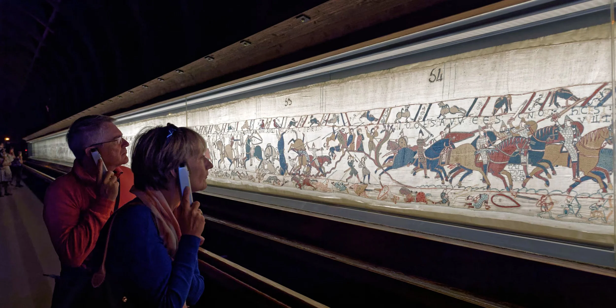 Two visitors study the Bayeux Tapestry whilst listening to an audio commentary