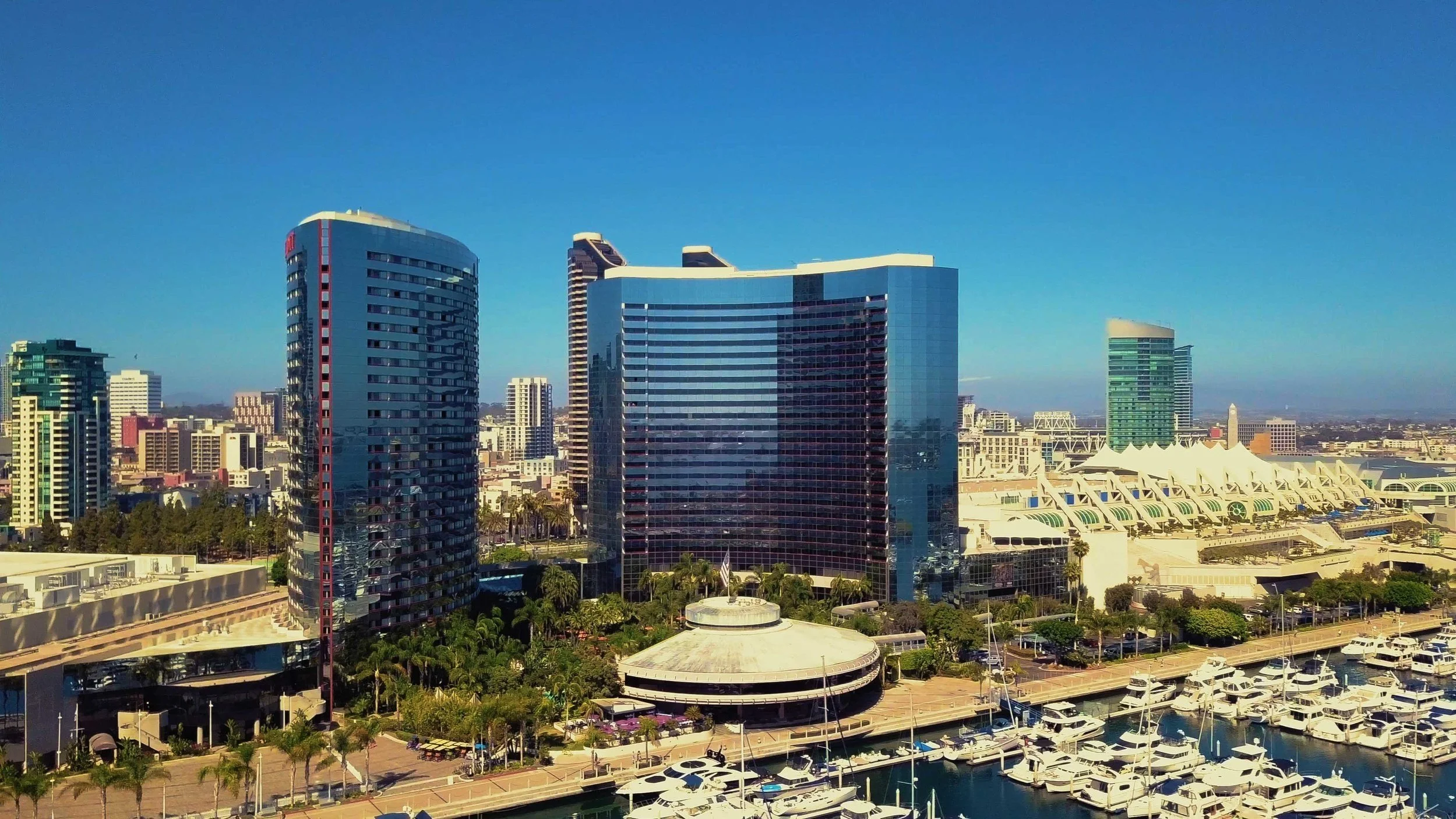City skyline featuring modern high-rise buildings, a marina with boats, and a waterfront area.