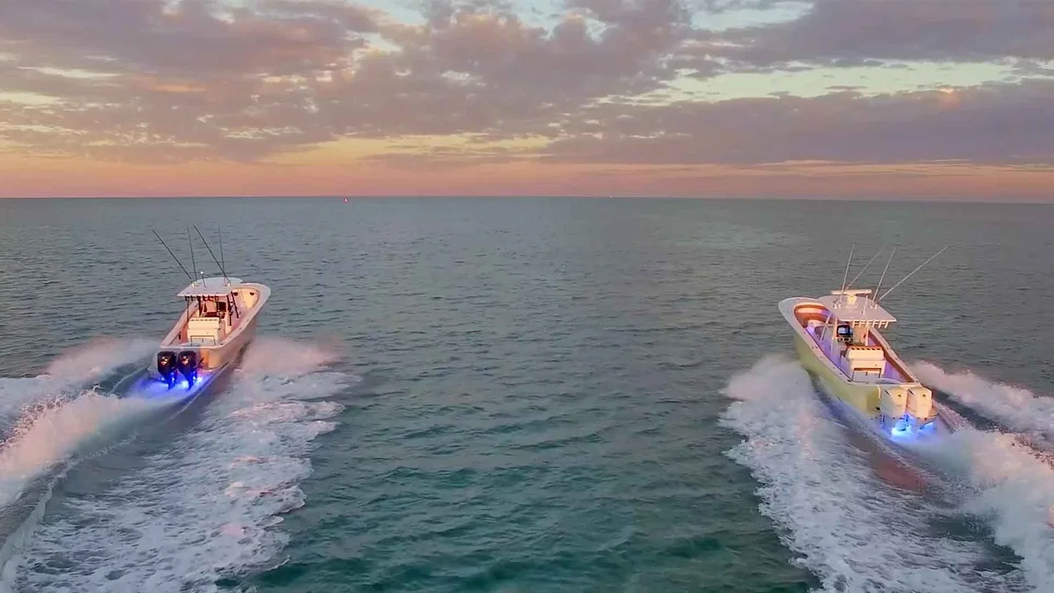 Two speedboats with fishing rods on a calm sea at sunset.