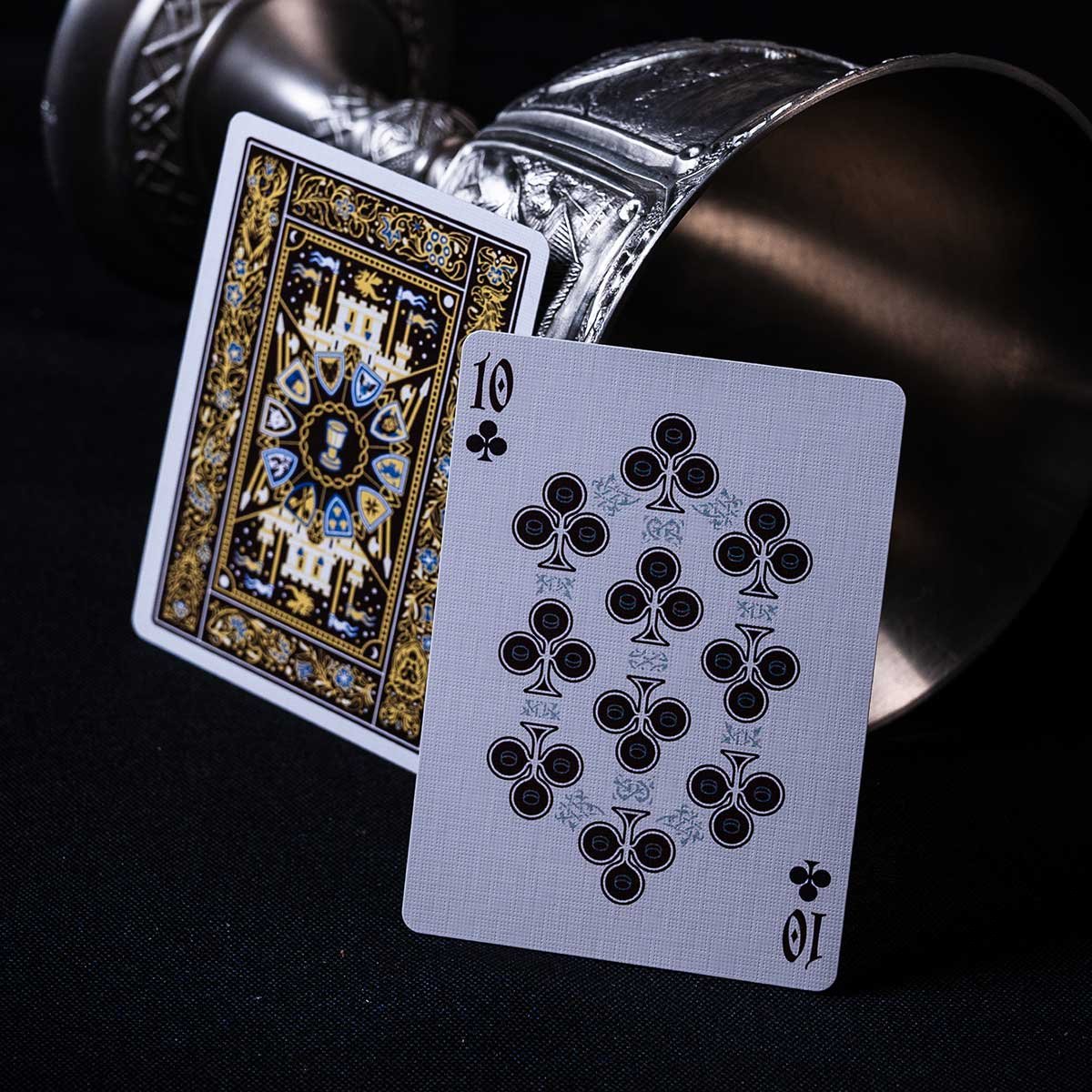 Ten of clubs and card back leaning on a pewter goblet tipped over