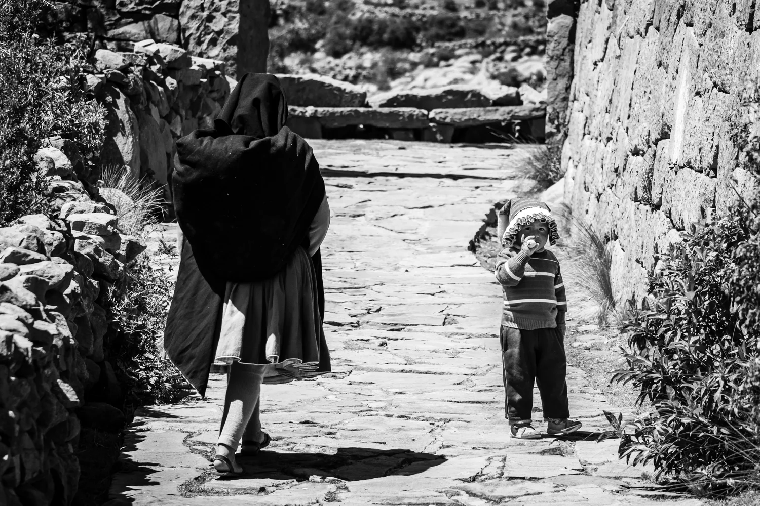 A little kid and her mother, walking on the narrow alleys of Taquile island on lake Titicaca. Young children are helping their families on the crop fields as well as by selling items to tourists.