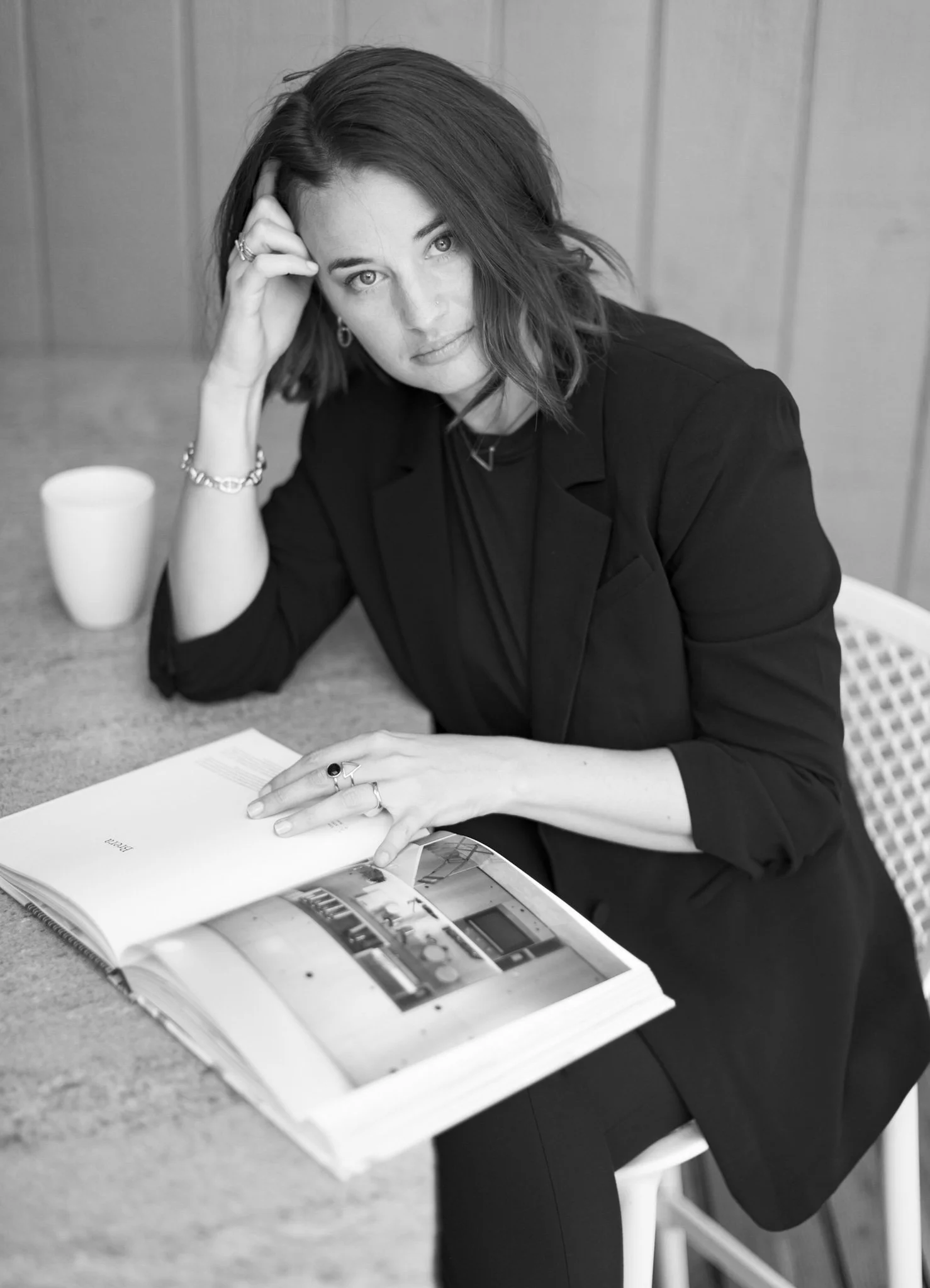 Black and white photo of a woman sitting at a table, resting her head on her hand, with a magazine or book open in front of her.
