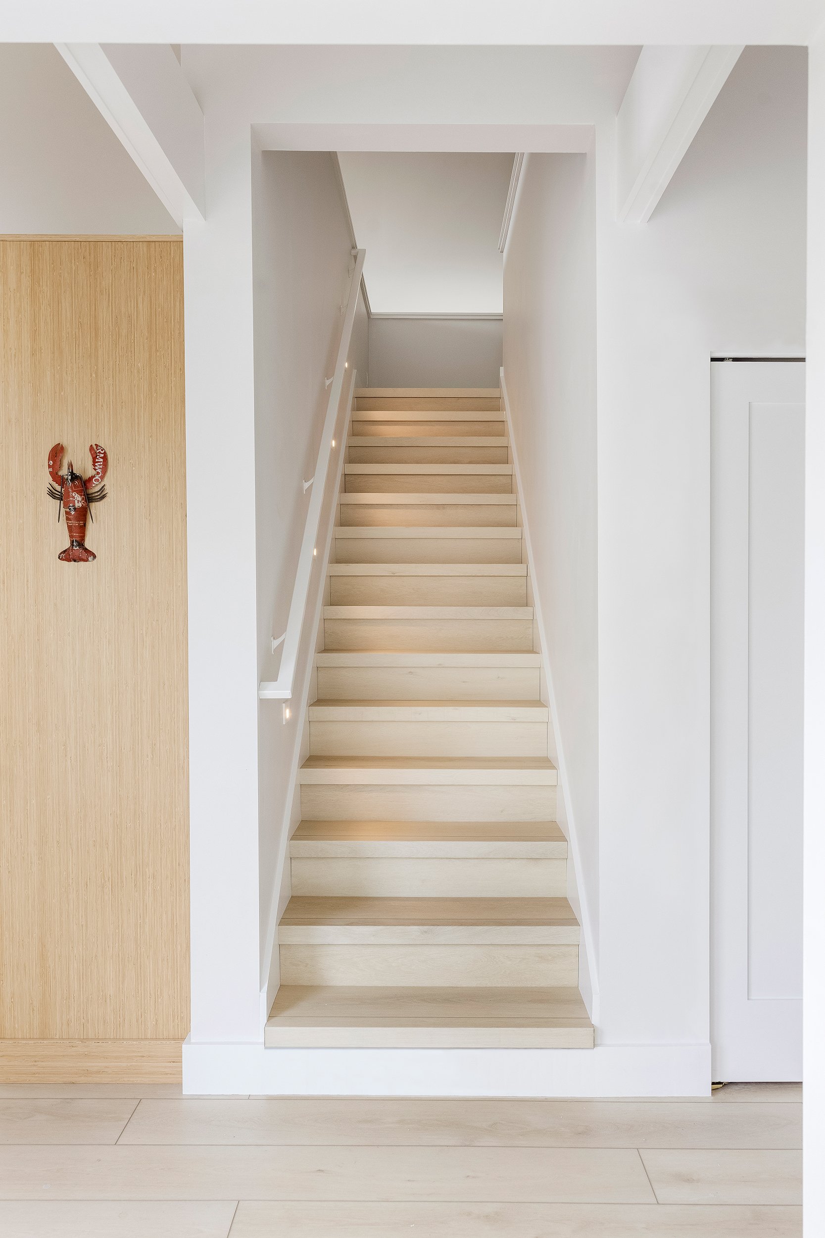 White staircase with wooden steps and a white handrail in a bright, modern interior.
