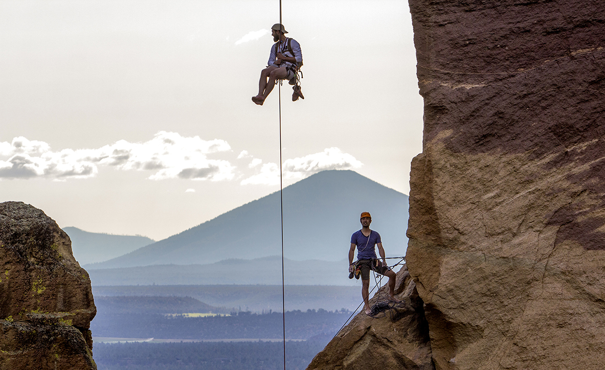 A rock climber descends down from the rock known as "Monkey Face" as another climbers looks on at Smith Rock State Park. Monkey Face is a 350 foot pillar, that resembles a monkey from the correct angle. The pillar contains several of the most difficult climbs in the world, including "just do it," and the "east face" crack. The "just do it" route is also the first 5.14c rated climb in the United States, an elite level grade in rock climbing. 