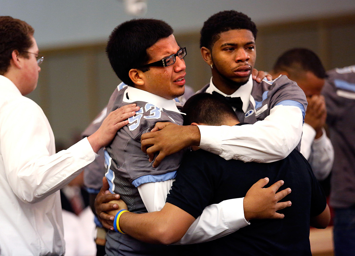 Javier Medina, 17, left, hugs his fellow Rebels teammates during the funeral for South High School's football coach John Wren at The Church of Jesus Christ of Latter-Day Saints in Bakersfield, Calif. John Wren, 44, who was considered both a father figure and mentor to the team, died unexpectedly in his sleep a week prior.