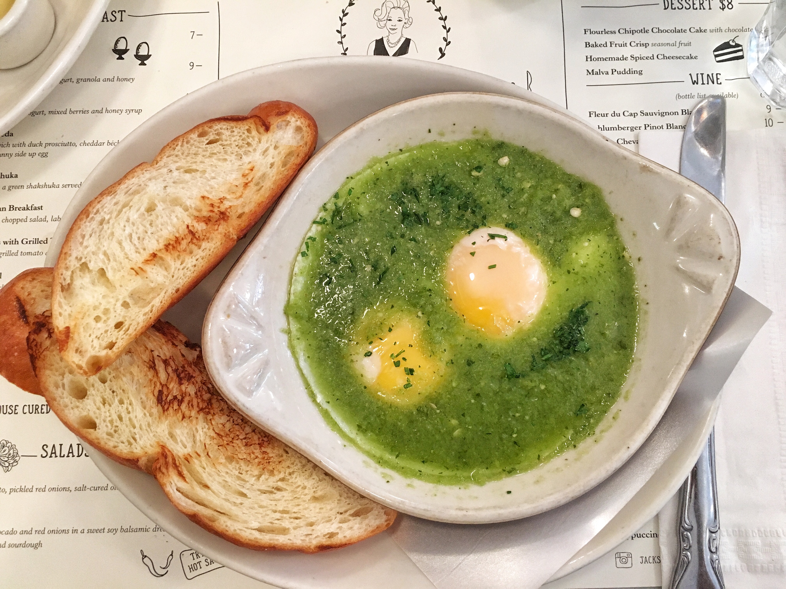 Green shakshuka with two poached eggs and challah bread