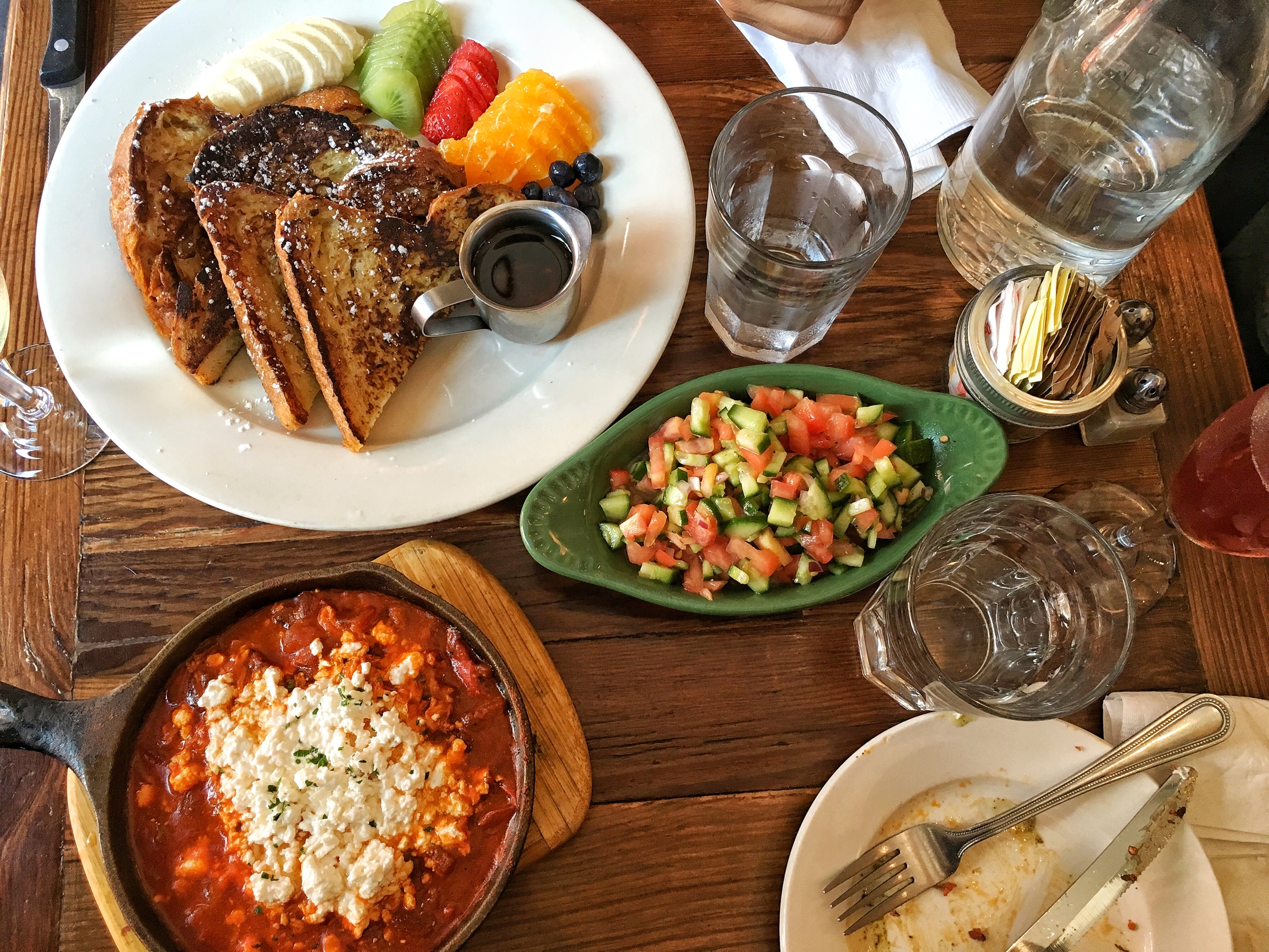 Shakshuka with two baked eggs and feta cheese, Israeli salad, Challah bread french toast with selection of fruits 