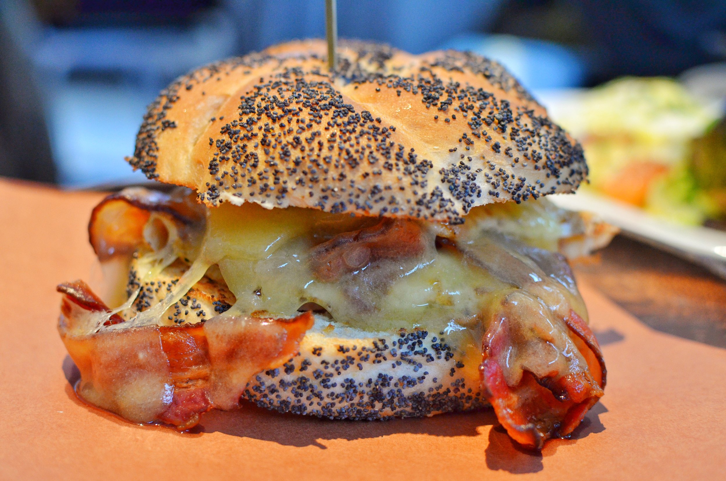 Egg sandwich with bacon, two fried eggs, melted cheddar cheese, pesto on a poppy seed Kaiser roll