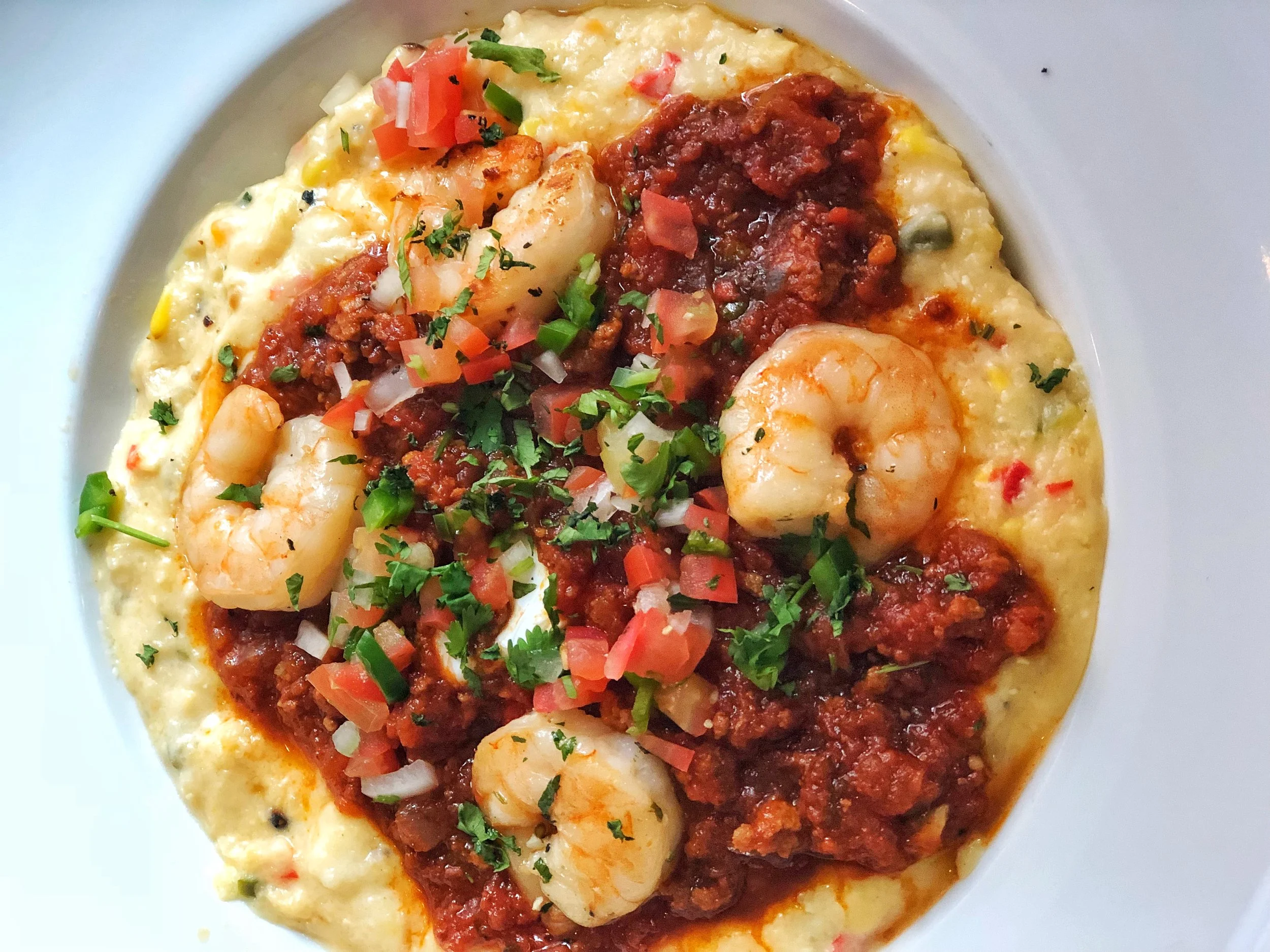 Shrimp and Grits with grilled heirloom cheddar grit cakes, poached egg, grilled shrimp, chorizo and red chili sauce