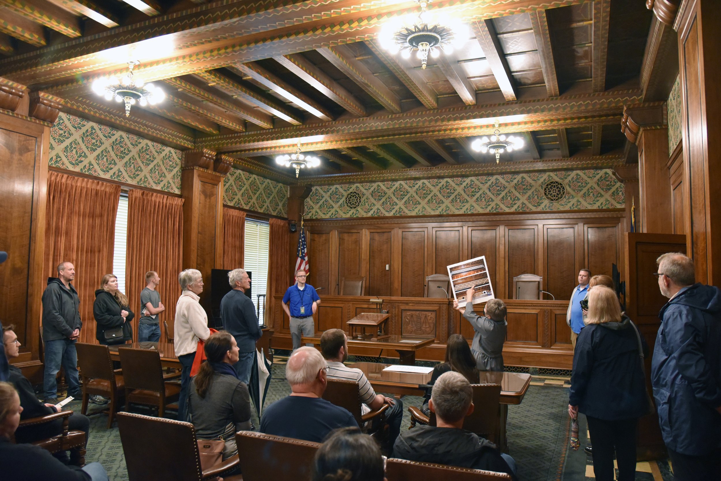 Capitol Tourism Supervisor Roxanne Smith points to a photograph of the heating and air-conditioning registers that existed high on the walls of the Court of Appeals Chamber before the new HVAC system was installed and the room meticulously restored.