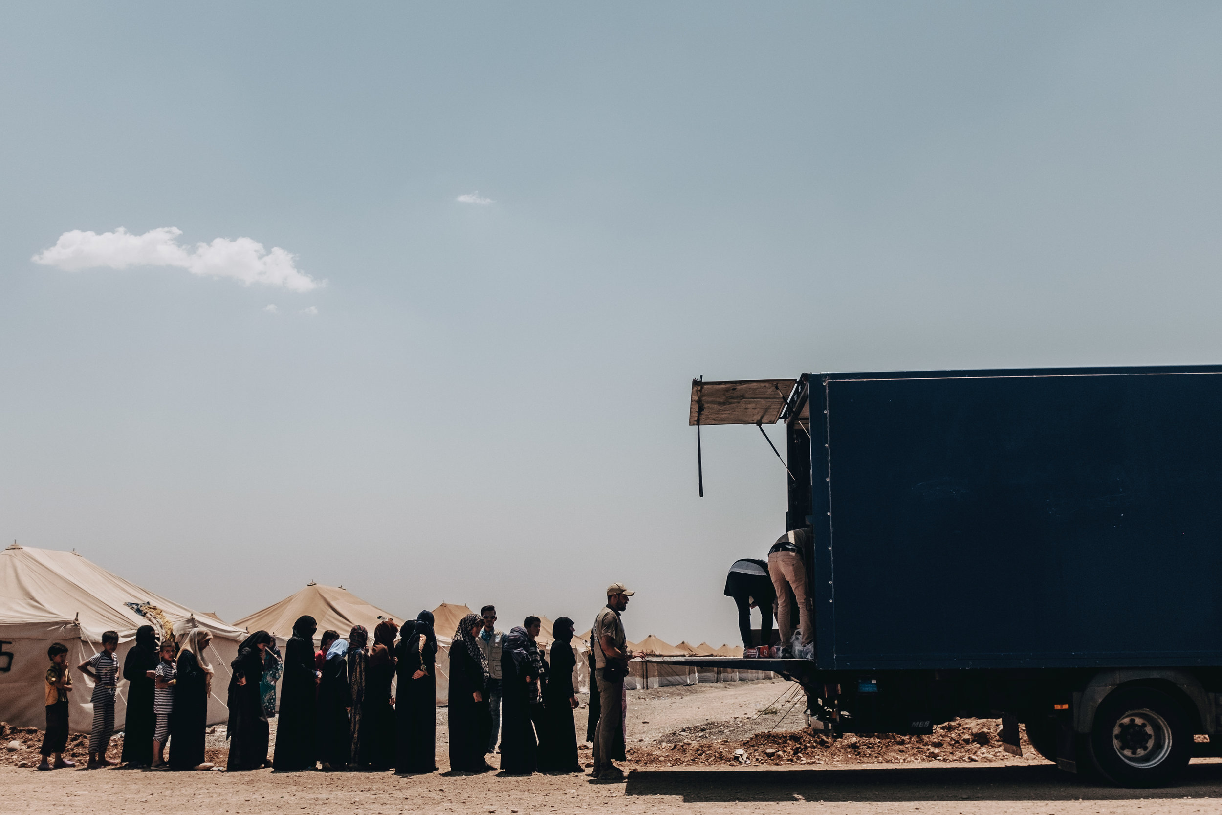 Residents of the camp stand in line and wait to recieve basic supplies such as tooth brushes, nappies and baby formula from the back of a truck operated by the One World Medical Mission.