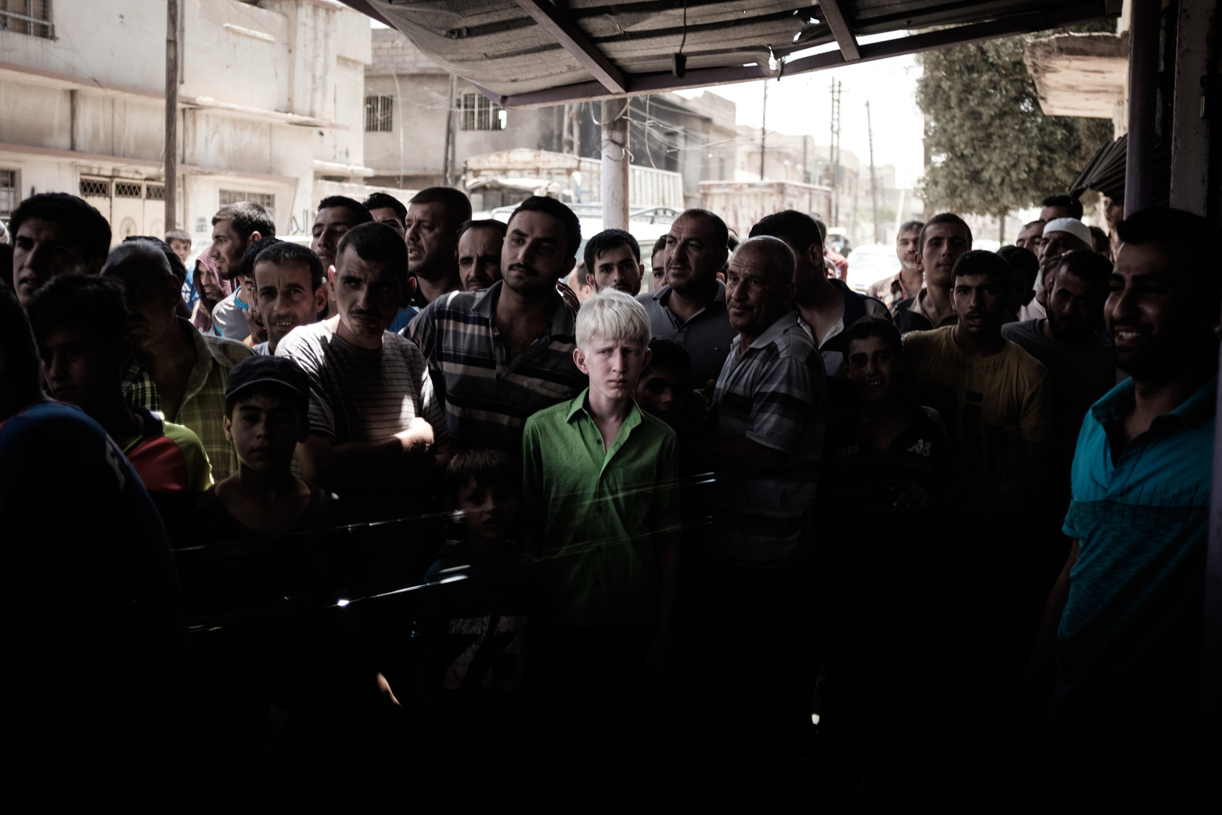 A boy with albinism stands in a crowd of people from his neighbourhood in West Mosul awaiting aid distribution from a local NGO. Since the fighting pushed through the area and into the Old City, this was the first humanitarian aid convoy to arrive in the area in a number of weeks. 