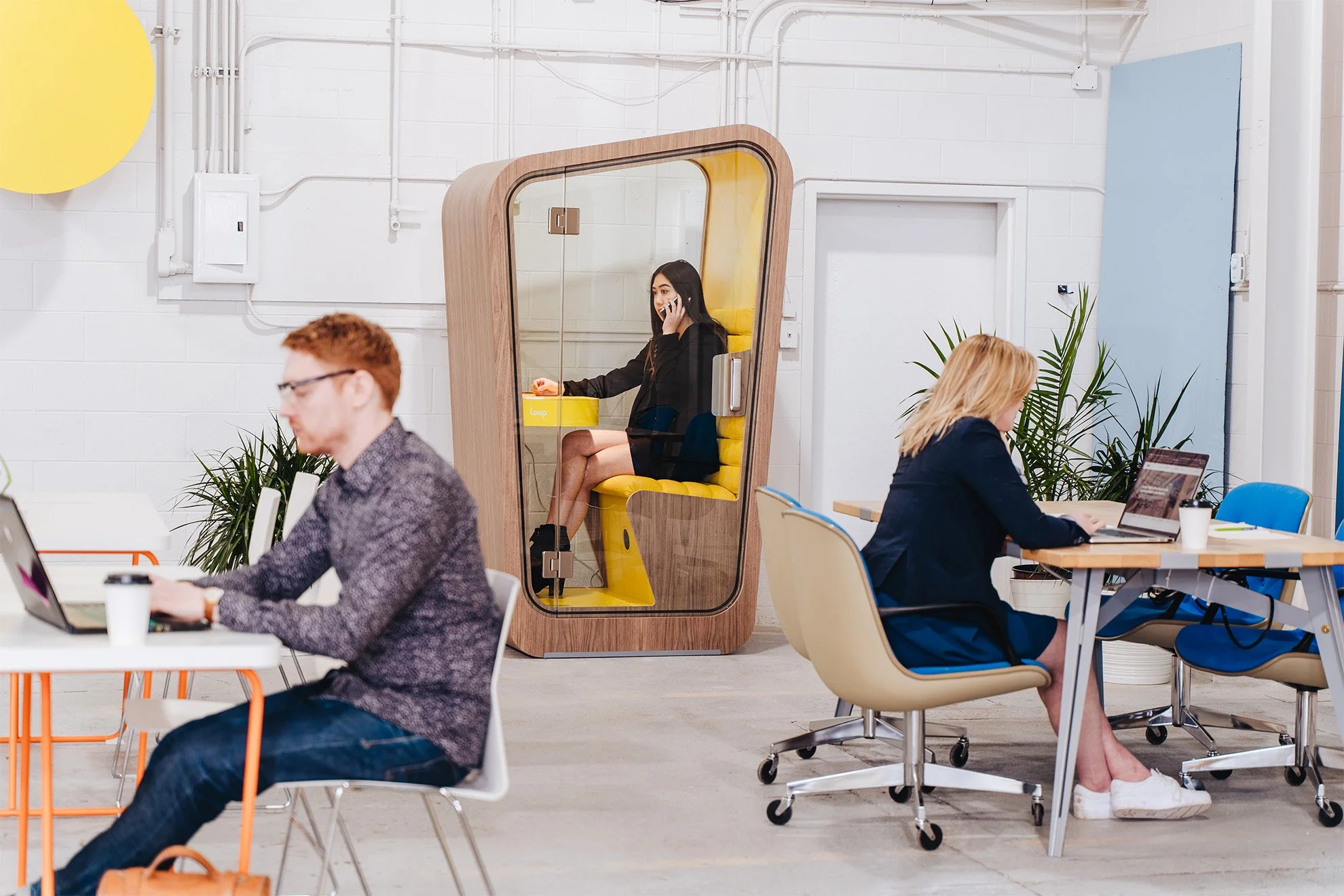a-woman-takes-a-phone-call-in-privacy-using-loop-solo-phone-booth-at-her-office-with-co-workers-working-at-desks-around-her.jpg