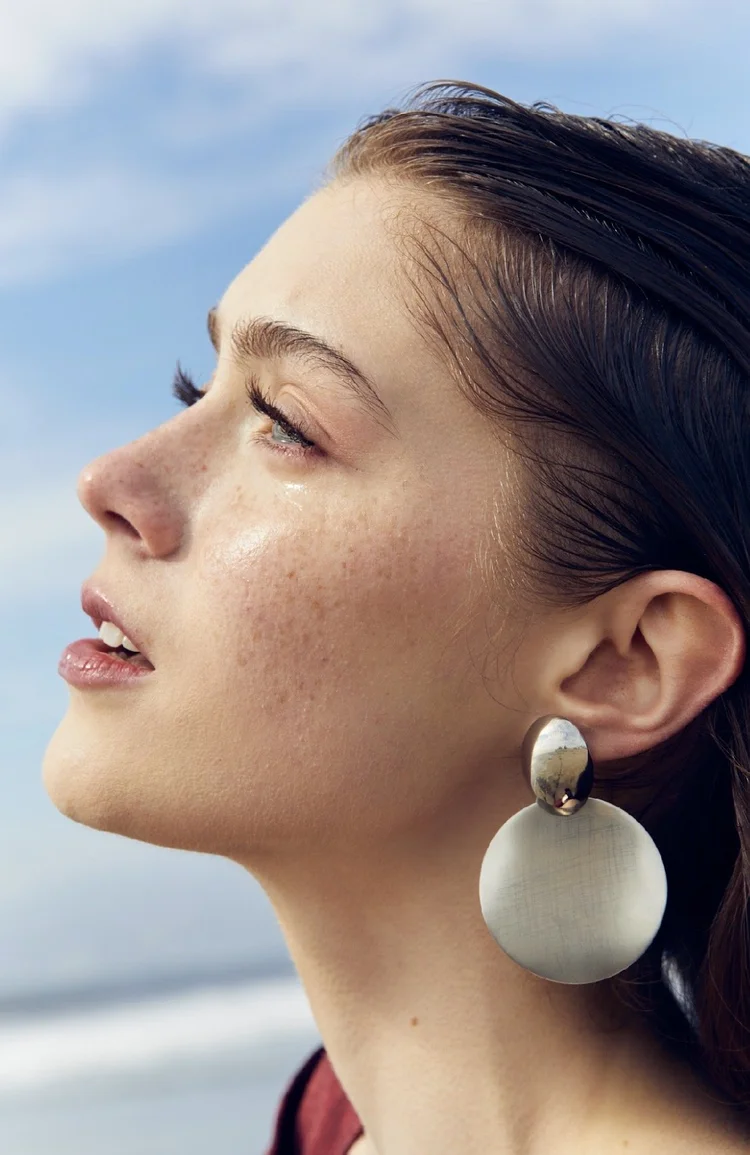 Outdoor beauty portrait with slicked-back dark hair and large white earrings