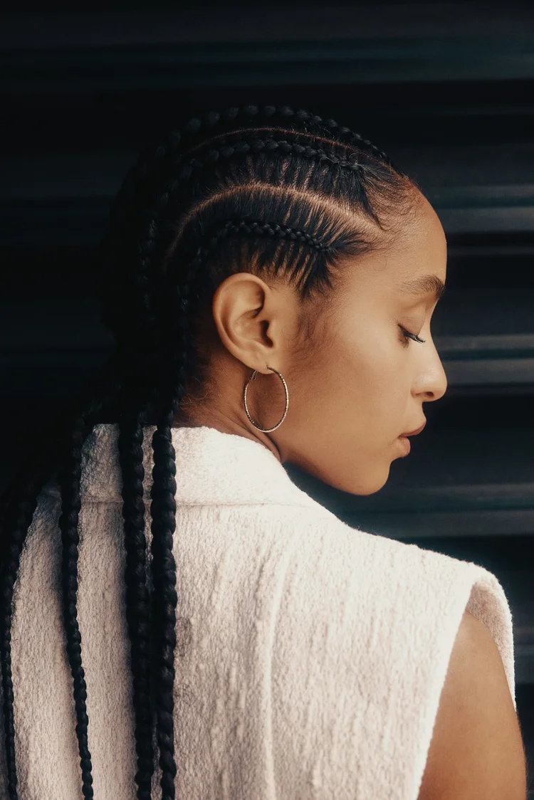 Profile showing precise cornrows flowing into long braids with a white sleeveless top