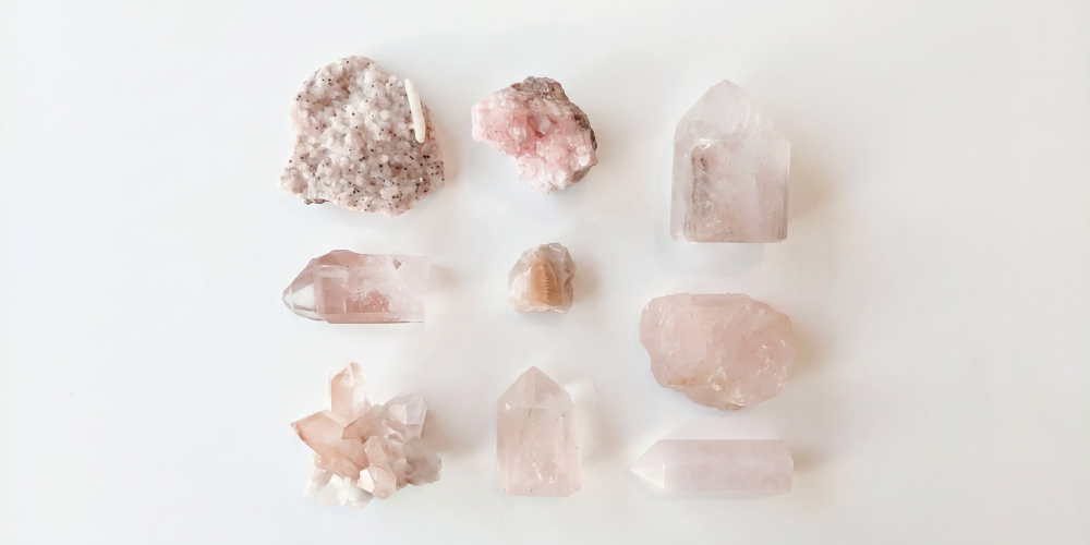 Arrangement of pale pink and white crystals, including rough and polished stones, displayed on a white background with a soft, serene tone.