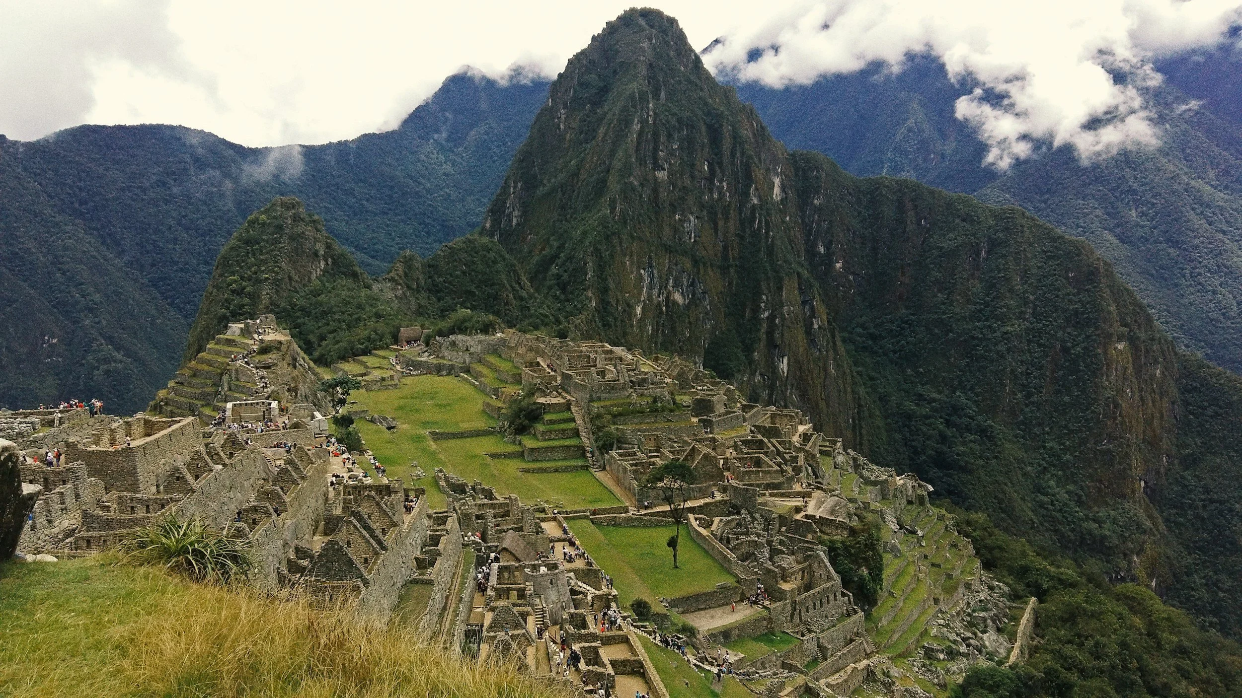 Aerial view of Machu Picchu, showcasing ancient stone ruins and terraces against lush green mountains, conveying a sense of historical grandeur and mystery.