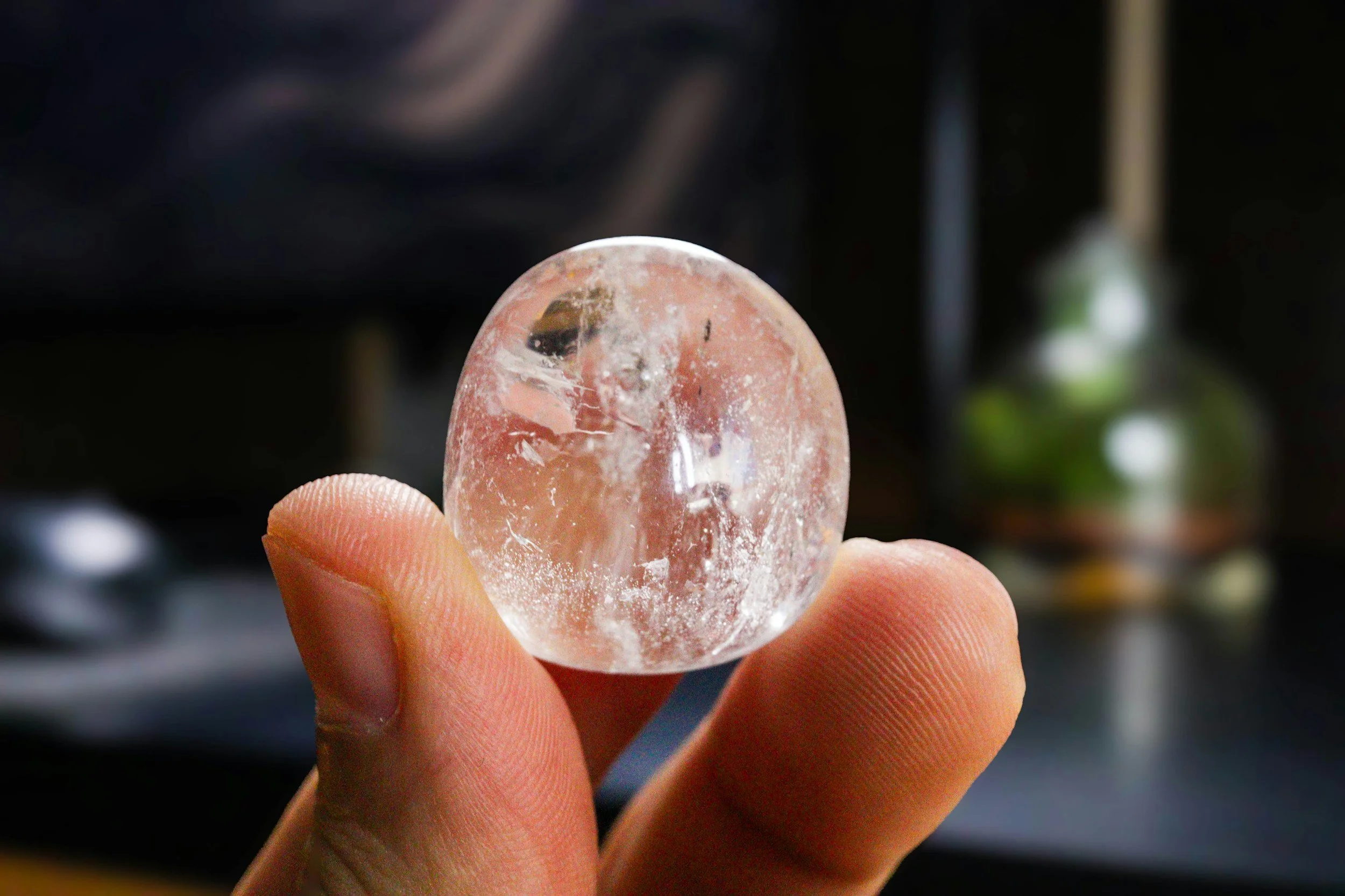 A hand holds a translucent, oval stone with a white circular mark. The background is blurred, hinting at a modern, softly lit interior space.