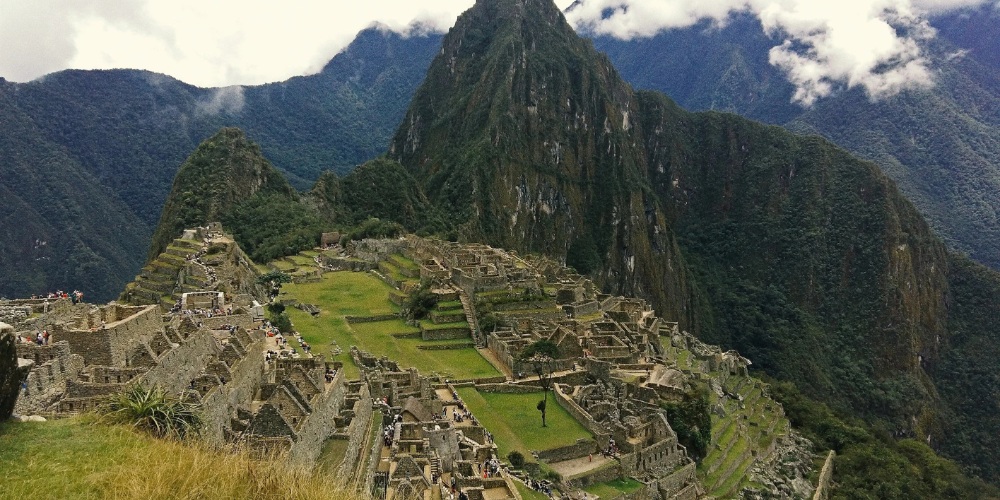 Aerial view of Machu Picchu, showcasing ancient stone ruins and terraces against lush green mountains, conveying a sense of historical grandeur and mystery.