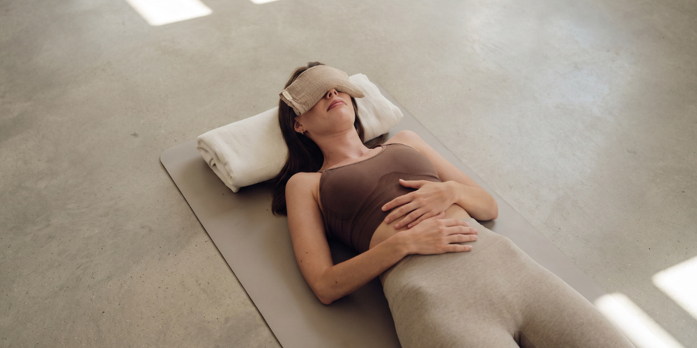 Woman resting comfortably on a mat with an eye mask while practicing relaxation and breathwork.