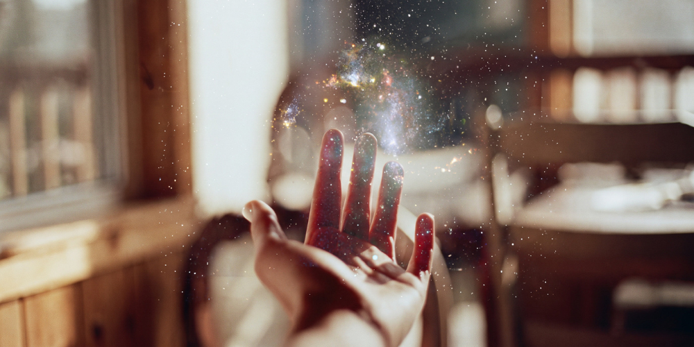 Open hand reaches upward as glowing golden sparkles swirl above the palm in a warm, softly lit room, creating a magical, hopeful mood.