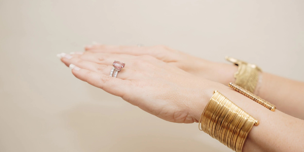 Close-up of an outstretched hand wearing a delicate ring and layered gold bangles, creating an elegant, luxurious fashion mood.