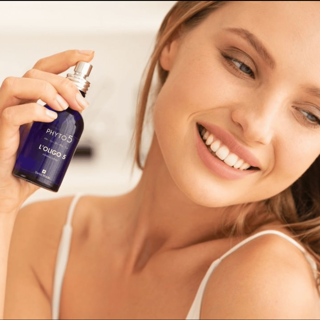 A woman sprays a mist of Oligo5 trace mineral spray onto her face