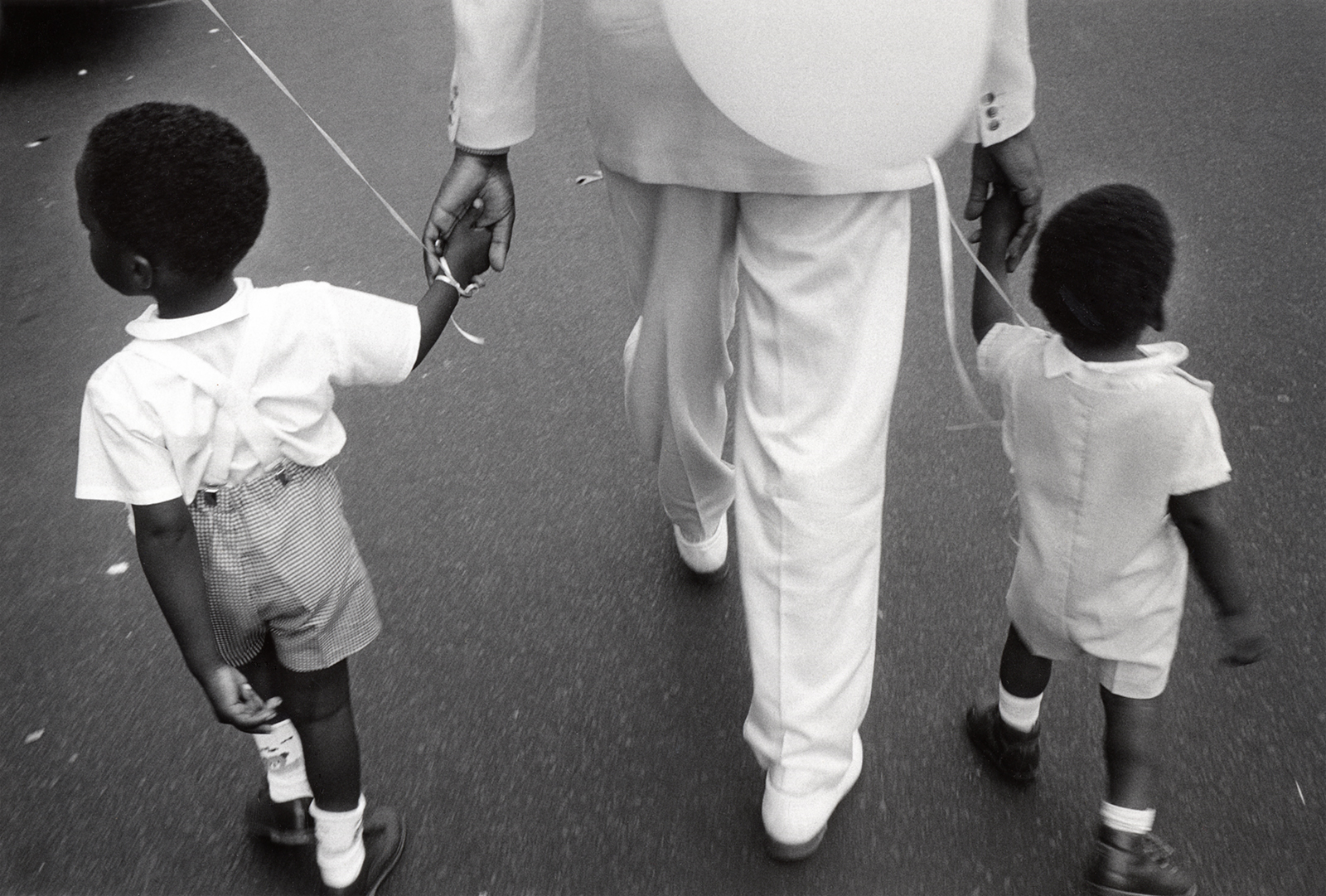 A father takes his two small sons to the Harlem Day Festival after church, 1988