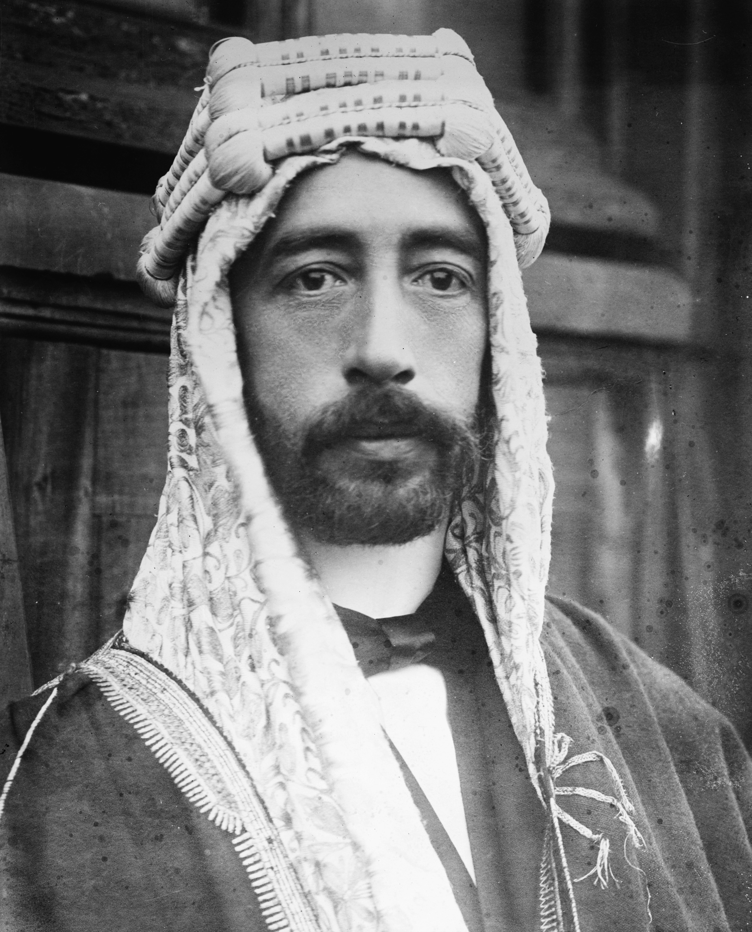 Undated image of King Faisal, probably from the early 1920s. A tall man of handsome, striking appearance, he was described thus by T. E. Lawrence on the occasion of their first meeting: " very tall and pillar-like, very slender, in his long white silk robes and his brown head-cloth bound with a brilliant scarlet and gold cord. His eyelids were dropped; and his black beard and colourless face were like a mask against the strange, still watchfulness of his body. " Originally he seems to have always dressed in Arab costume, even when visiting Europe, but at some point in the mid-1920s he switched to a more western sort of appearance, which is how he looks on the lower-value stamps here. ( Library of Congress )